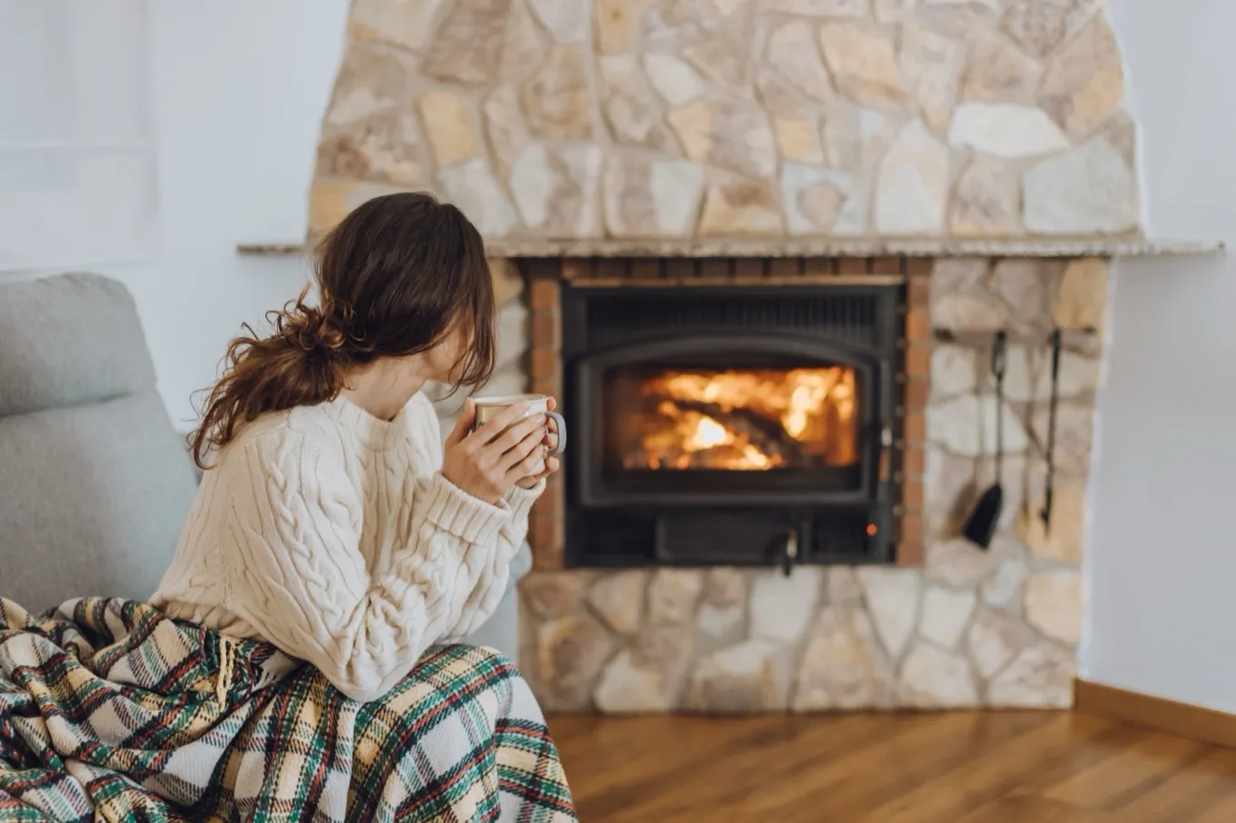 A homeowner with a mug of coffee in front of a stone fireplace with a wood insert burning.